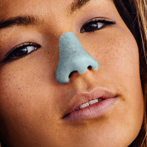 Asian woman wearing blue colored reef safe, eco friendly, and colorful vegan Nöz sunscreen.